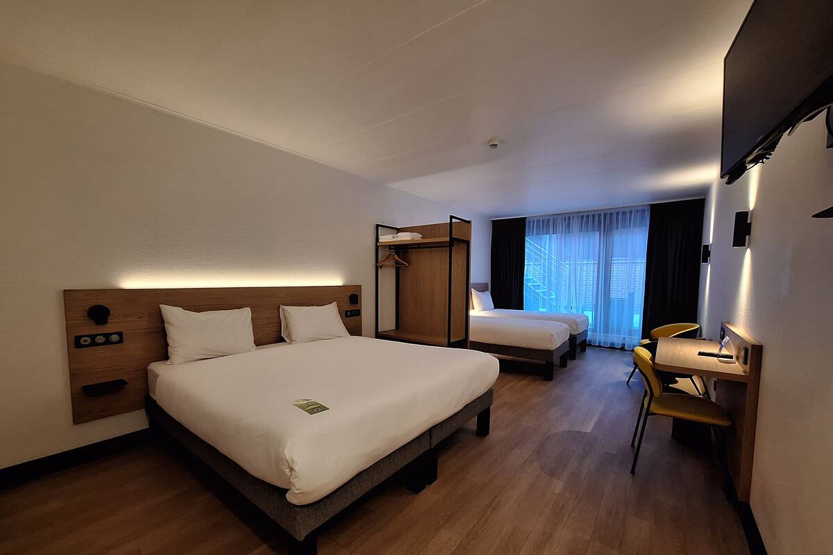 A hotel room with two beds, a desk, a chair, a wardrobe, and a window with curtains.