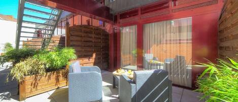 An outdoor patio with wicker furniture, a wooden planter with plants, and a brick wall.