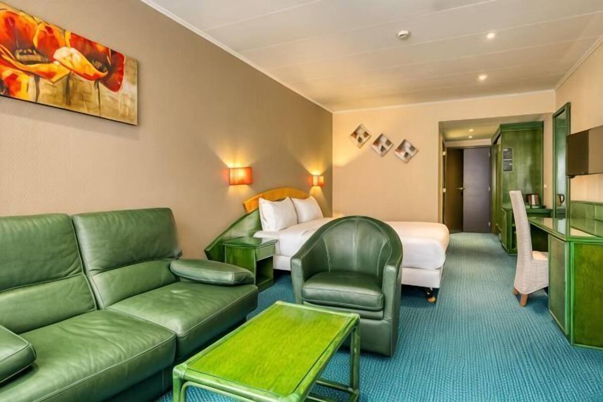 A hotel room with a green sofa, a bed, a green armchair, a small table, and a green cabinet.