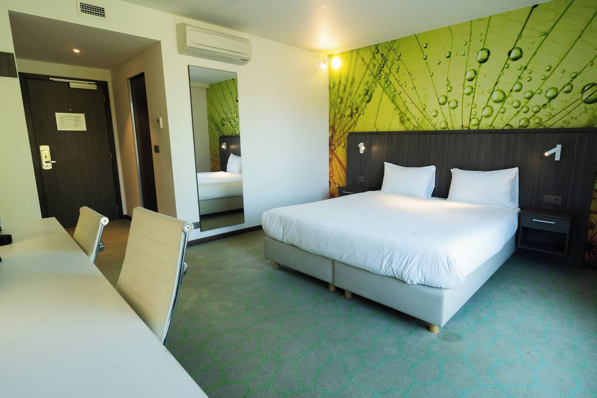 A hotel room with a large bed, a desk, and a mirror.