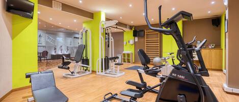 Un gimnasio con máquinas de cardio, una banca de pesas y un espejo.