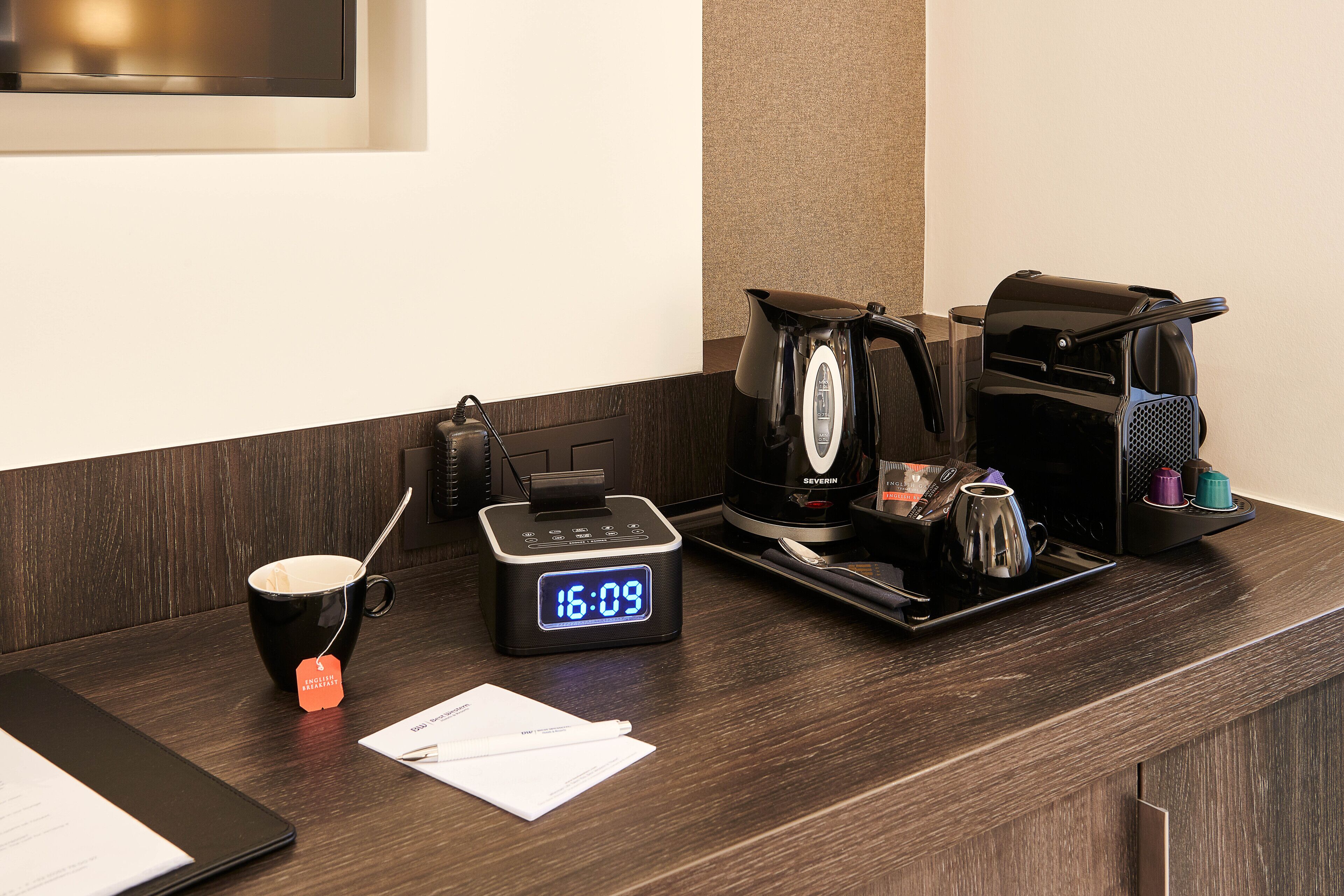 Una recepción de hotel con un reloj digital, una cafetera, una taza y una tableta.