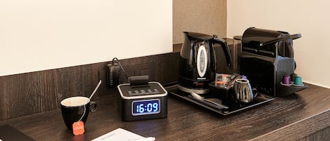 A hotel reception desk with a digital clock, a coffee maker, a mug, and a tablet.