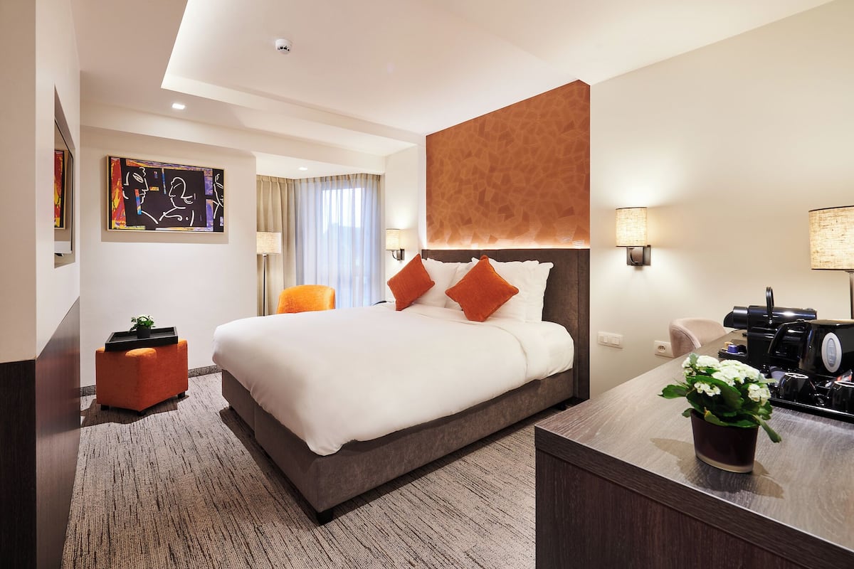 A modern hotel room with a large bed, a desk with a coffee maker, and a potted plant.