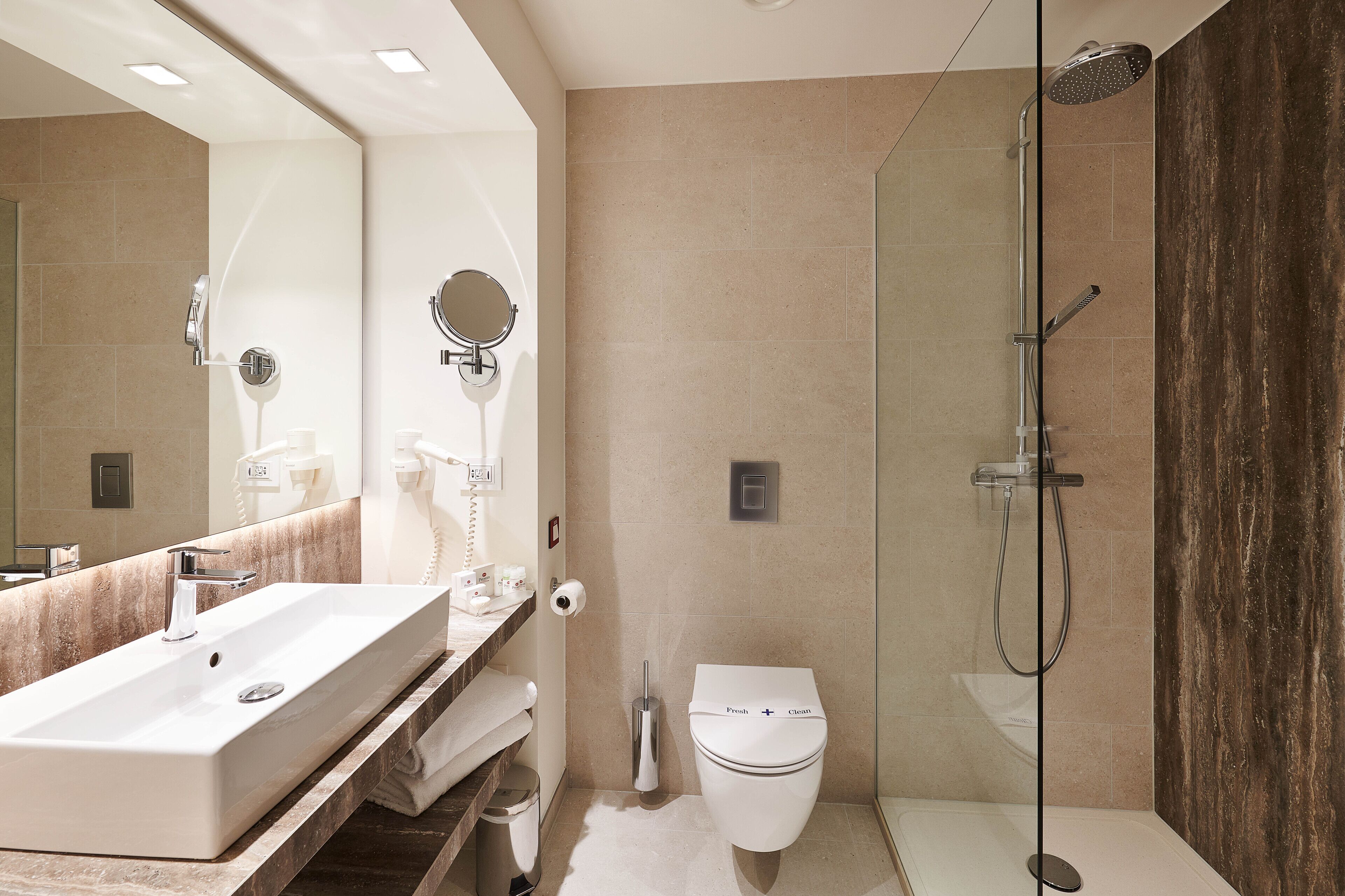 Un baño moderno con un lavamanos grande, espejo, inodoro y ducha con mampara de vidrio.