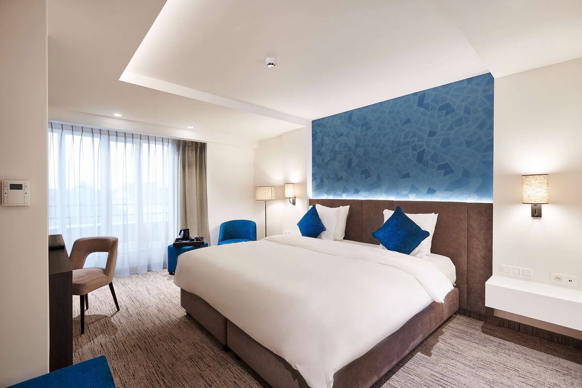 A hotel room with a large bed, a desk, a chair, and a bathroom with a mirror and sink.