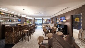 A modern bar area with a marble countertop, multiple seating options, and a television screen. - Keizershof Hotel (Aalst)