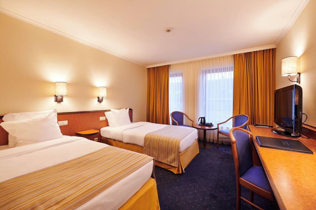 A hotel room with two beds, a desk, a chair, a television, and a small table.