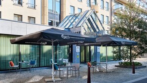 An outdoor seating area with a modern design, featuring a glass structure and branded umbrellas. - Keizershof Hotel (Aalst)