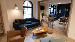 Een moderne woonkamer met een bank, salontafel en stoelen. Er is een groot raam en een aan de muur bevestigde televisie.
