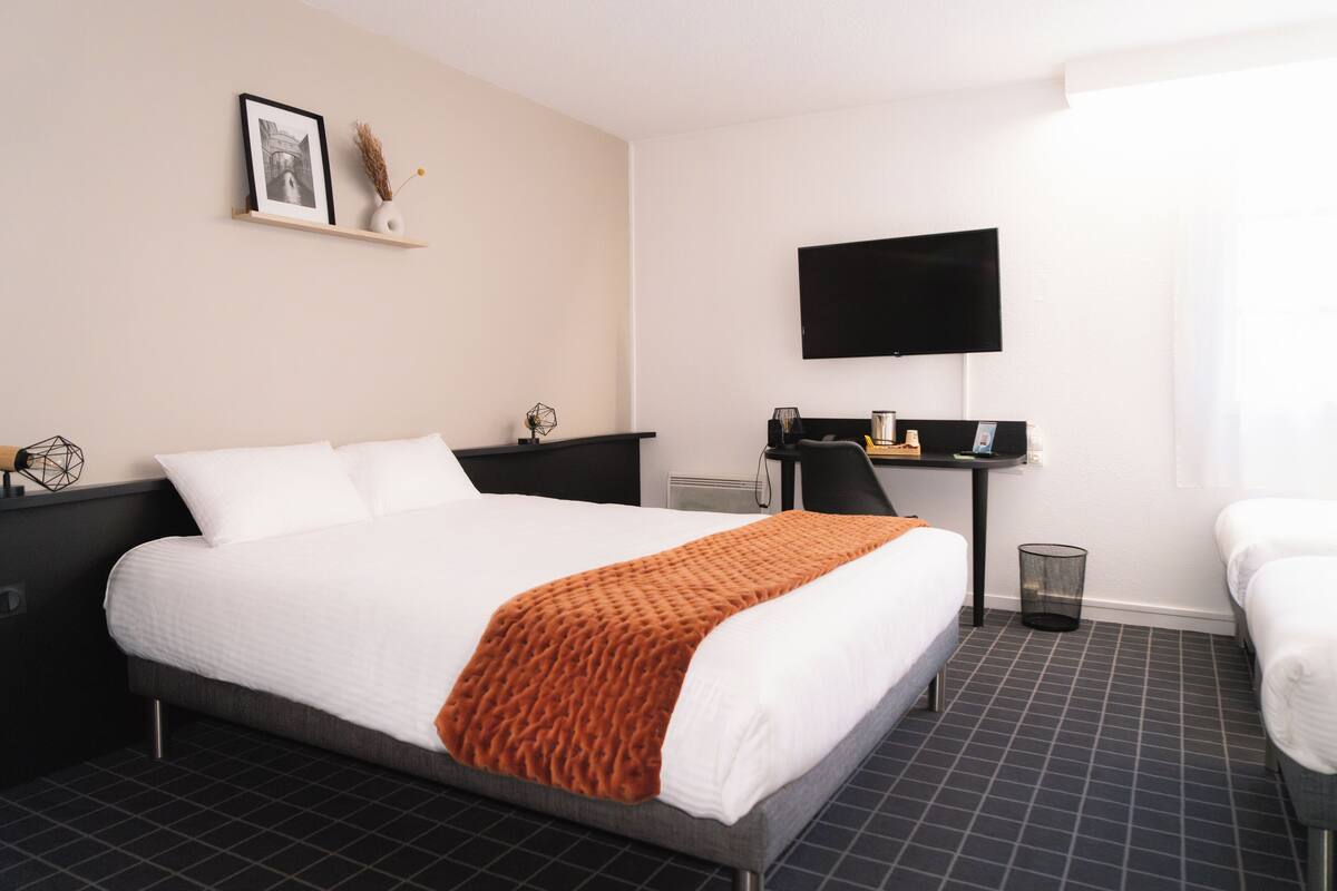 Ein Hotelzimmer mit einem großen Bett, einem Schreibtisch mit Stuhl, einem Fernseher und einer kleinen Mülleimer.