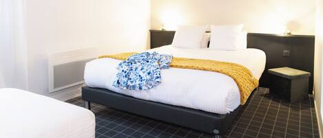 Una habitación de hotel con una cama, mesitas de noche y un par de zapatos en el suelo.