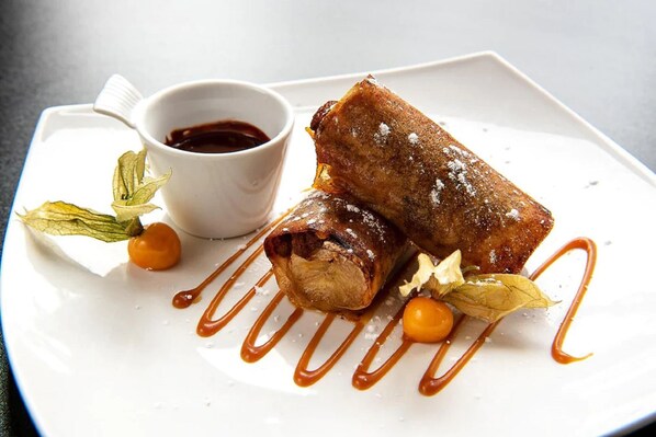 Un plato con dos rollos de hojaldre, un cuenco pequeño de salsa y hojas decorativas.