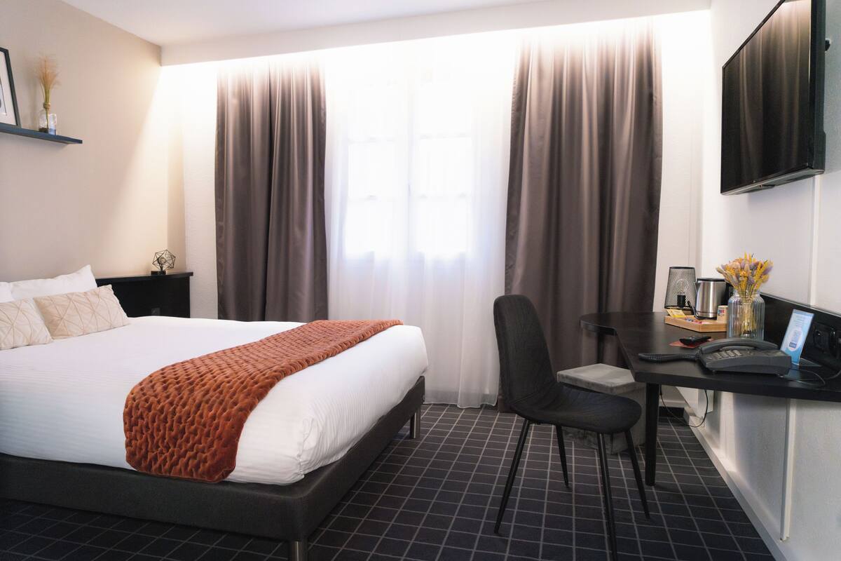 Ein Hotelzimmer mit Bett, Schreibtisch mit Computer, Stuhl und Fernseher an der Wand.