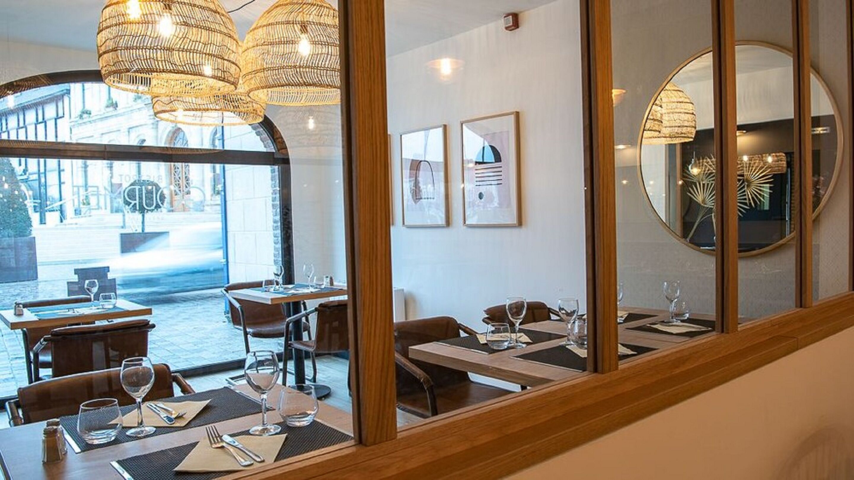 A restaurant interior with wooden tables, chairs, and hanging wicker chandeliers.