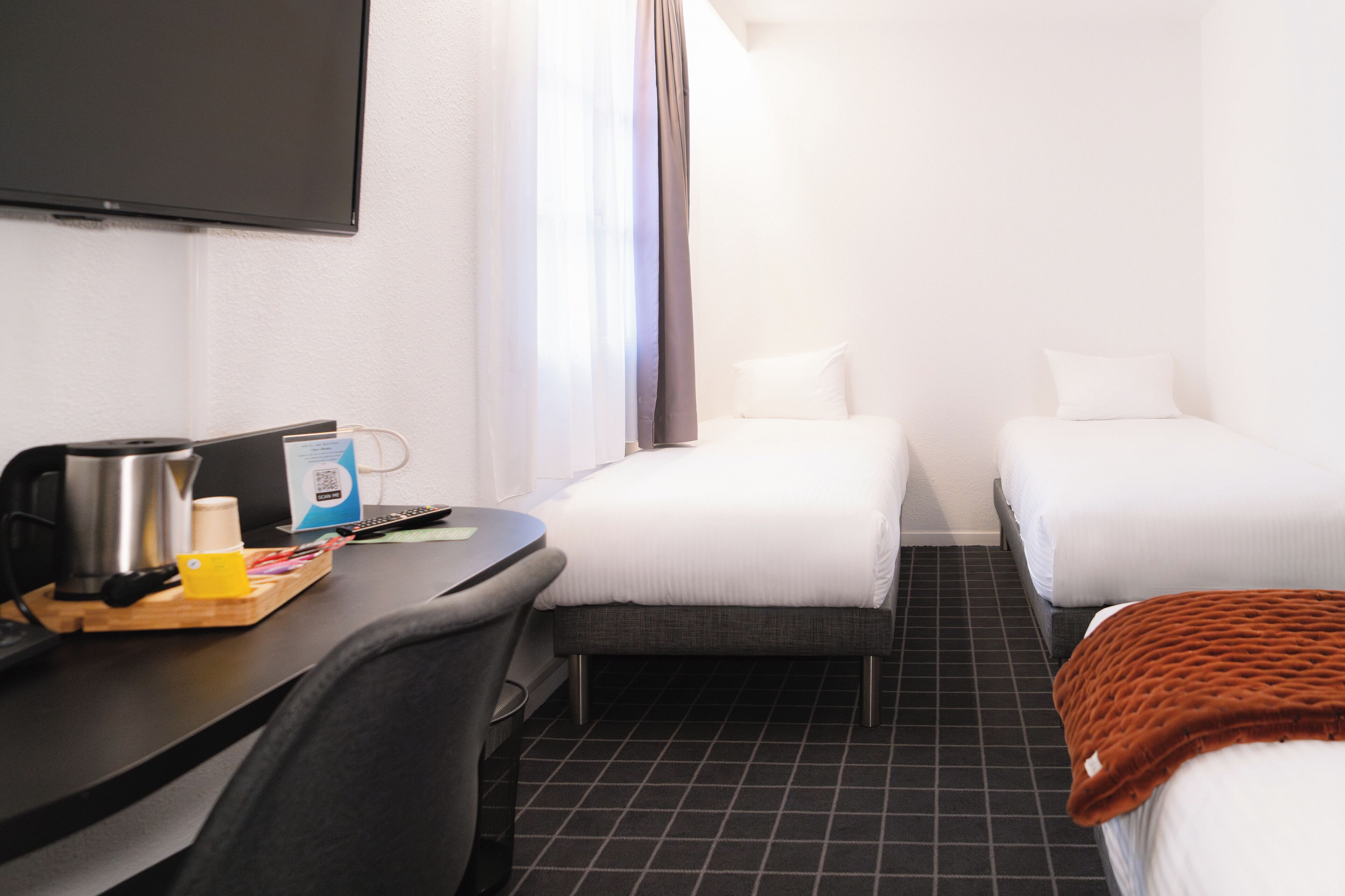 A hotel room with a desk, two beds, a TV, and a coffee maker.