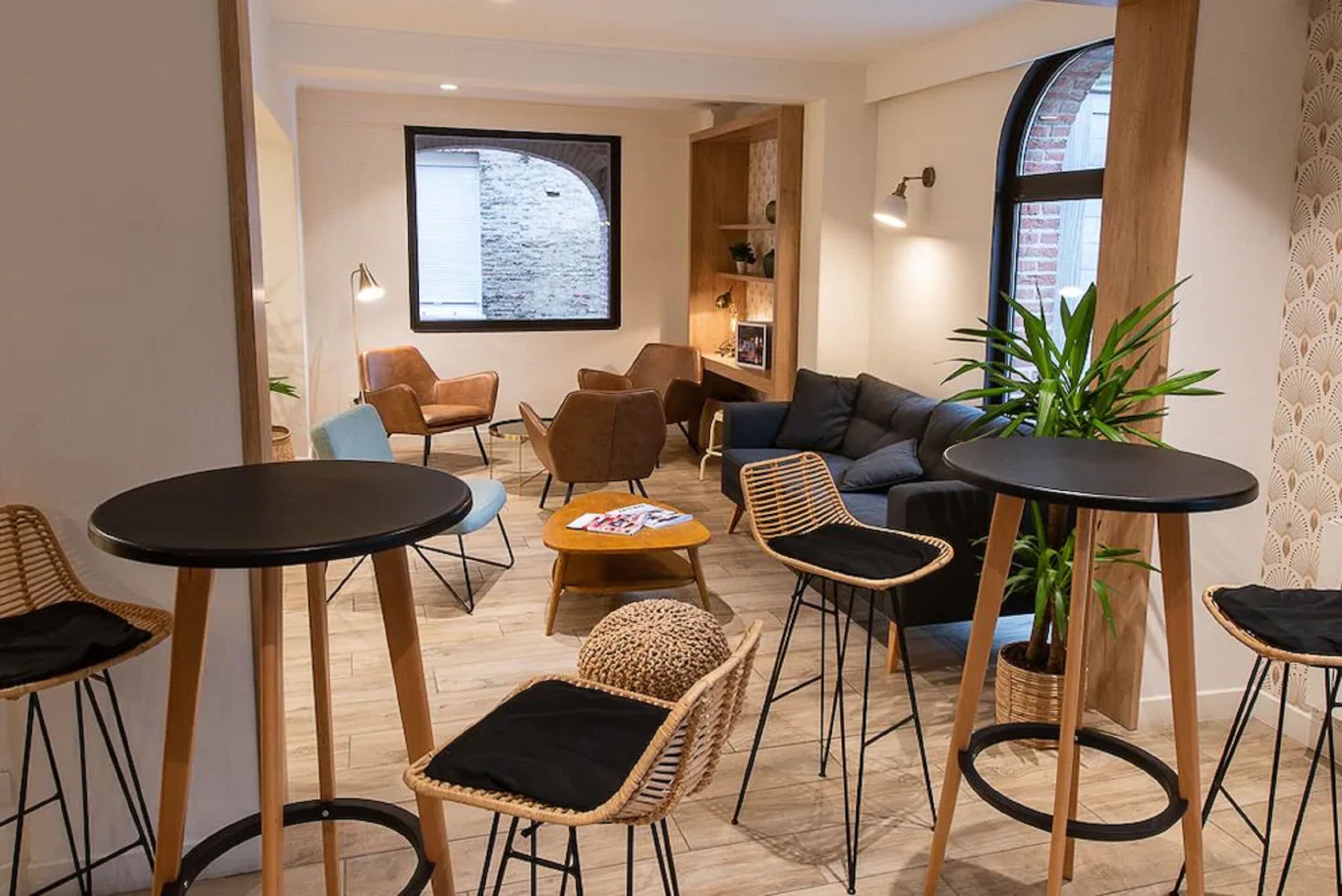 Un salon moderne avec un canapé, des fauteuils et une table basse. Une grande fenêtre offre une vue sur un mur de briques.