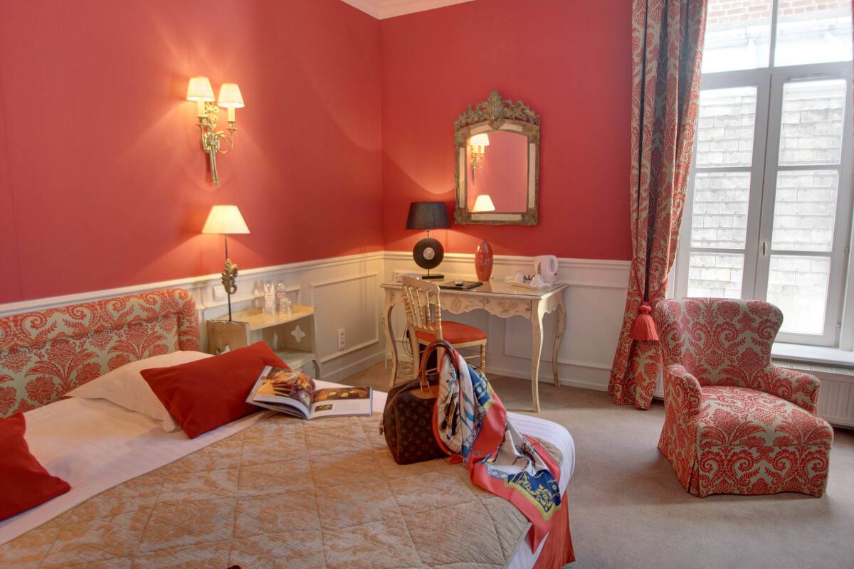 A hotel room with a bed, a desk, a chair, a mirror, and a window with curtains.