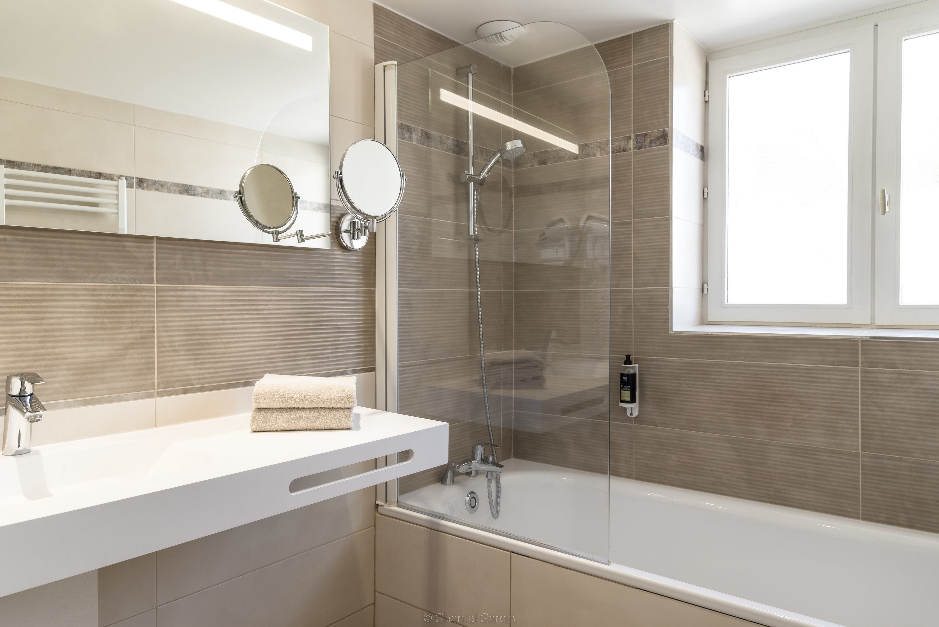A modern bathroom with a glass-enclosed shower, a white sink with a towel, and a large mirror.