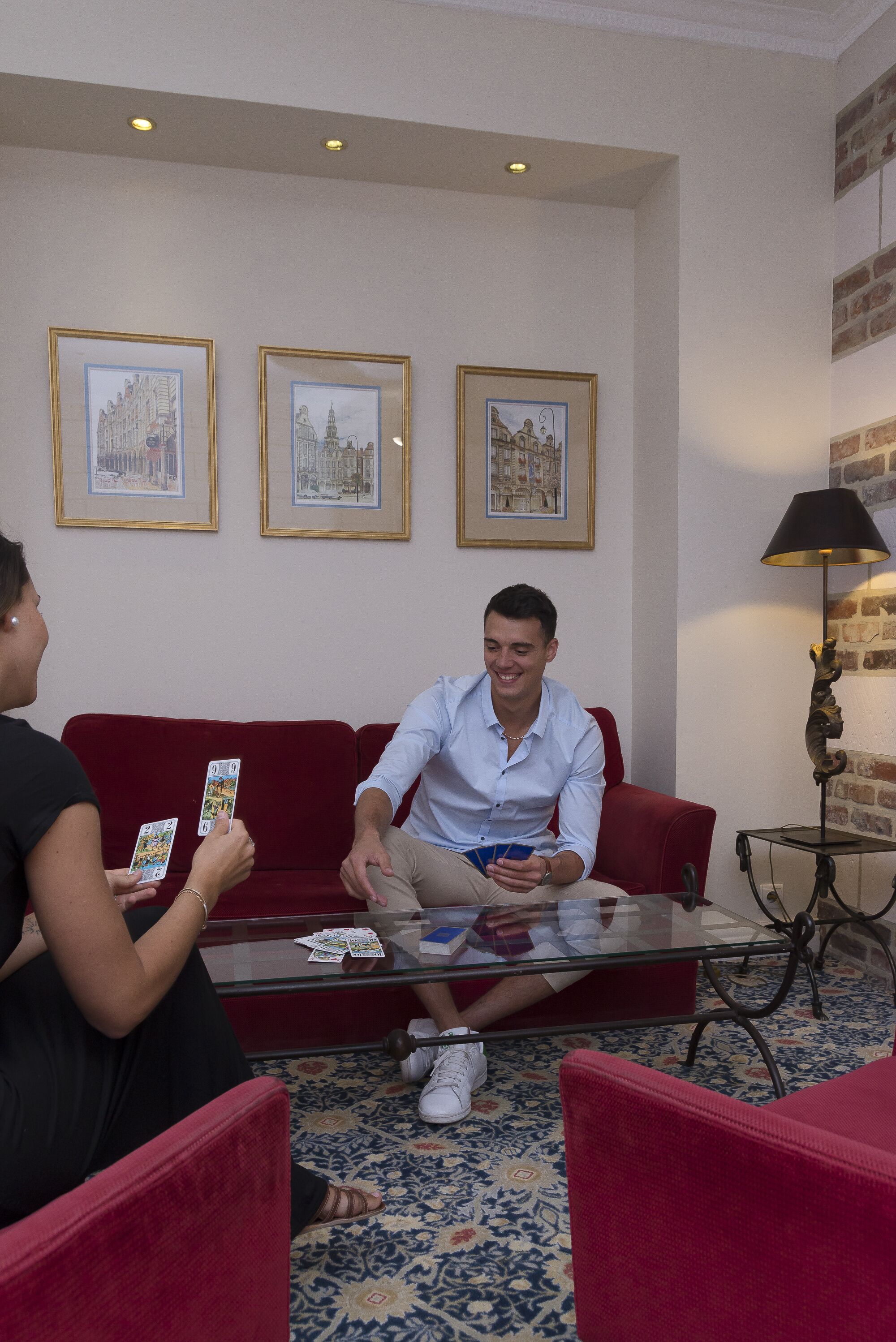 A red couch, a glass coffee table, and a lamp in a room with framed pictures on the wall.