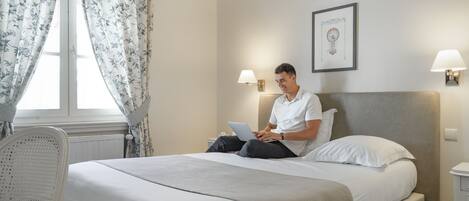 Una habitación de hotel con una cama, una silla, una computadora portátil y dos lámparas fijadas a la pared.