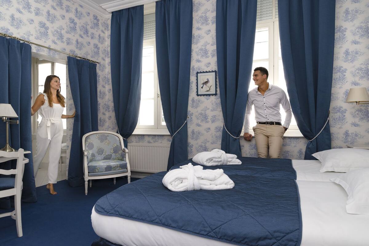 A hotel room with a large bed, a chair, and a window with curtains.