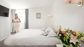 Een hotelkamer met een bed, een nachtkastje met een bloemenvaas, een wandlamp en een televisie aan de muur.