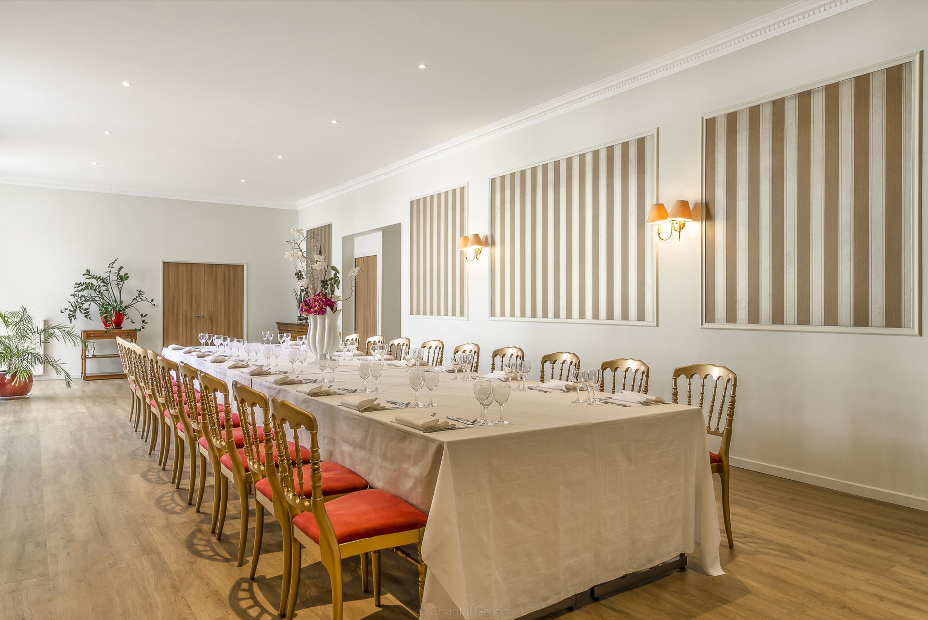 A long dining table set for a meal with chairs, a vase of flowers, and wall-mounted lamps.
