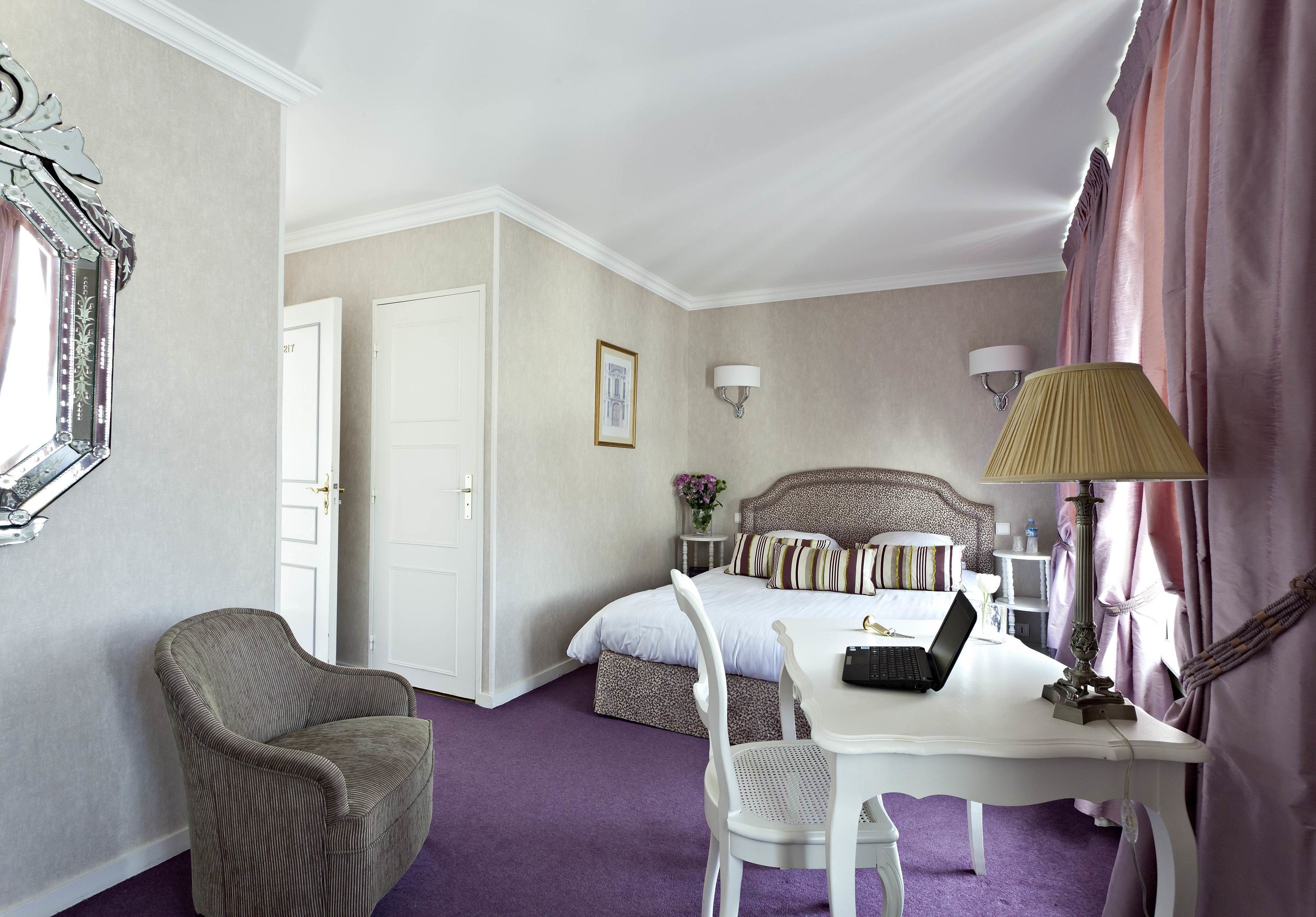Una habitación de hotel con una cama, un escritorio con una computadora portátil, una silla, una lámpara y un espejo.
