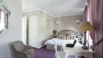 A hotel room with a bed, a desk with a laptop, a chair, a lamp, and a mirror.