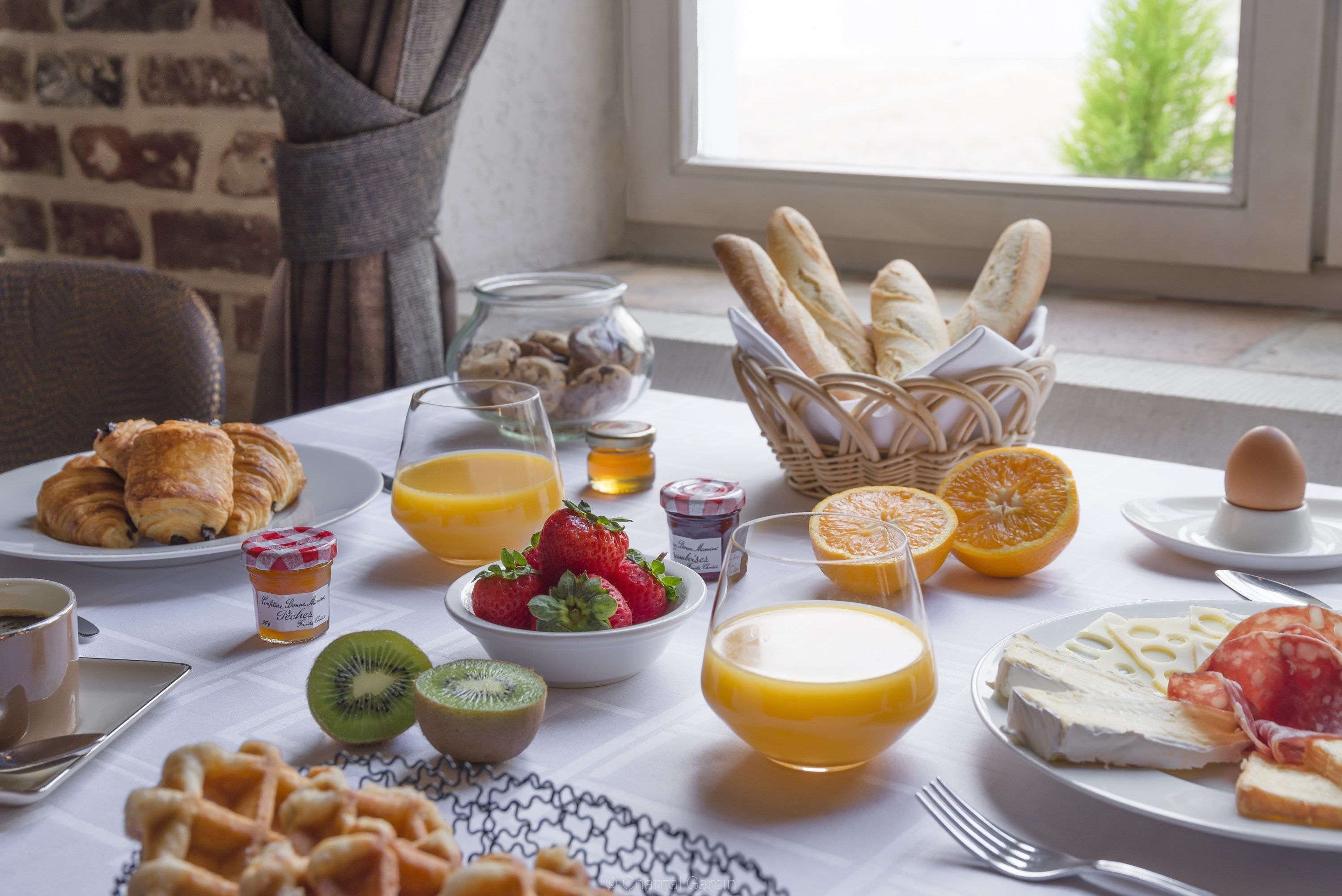 A breakfast table with croissants, strawberries, kiwi, orange juice, cheese, and bread.