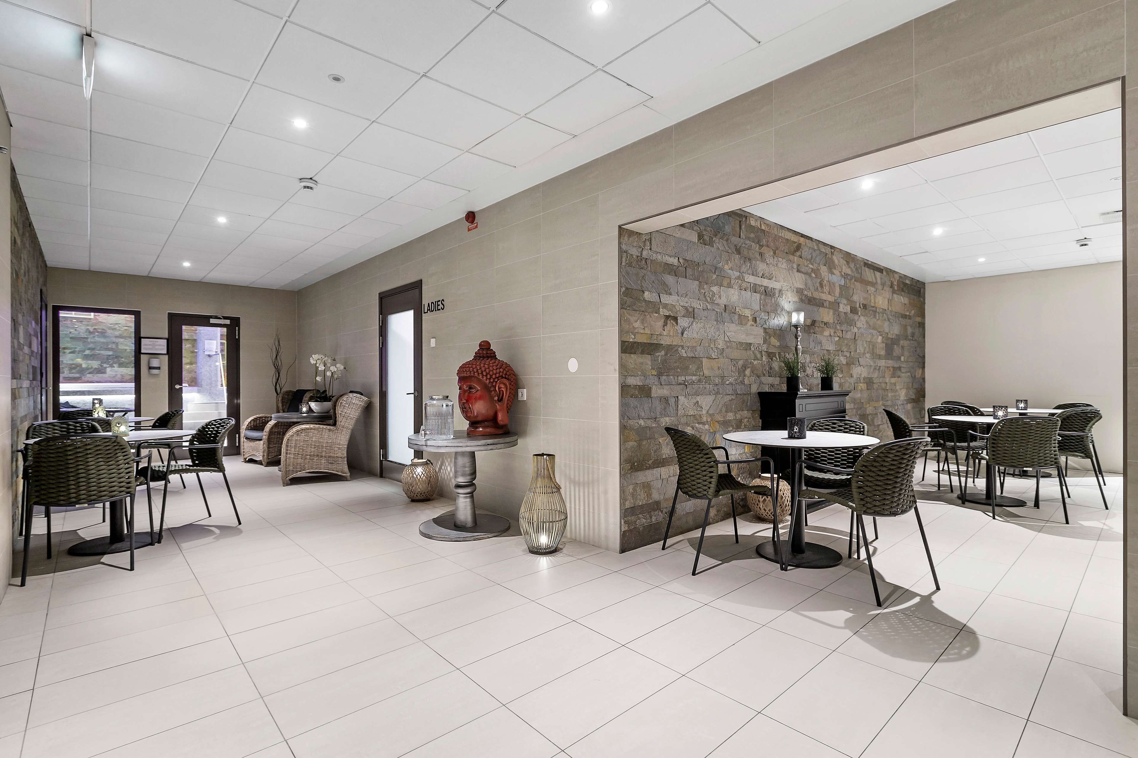 Un espace de restauration intérieur moderne, doté de nombreuses tables et chaises, d’un mur décoratif en pierre et offrant une vue sur l’extérieur.