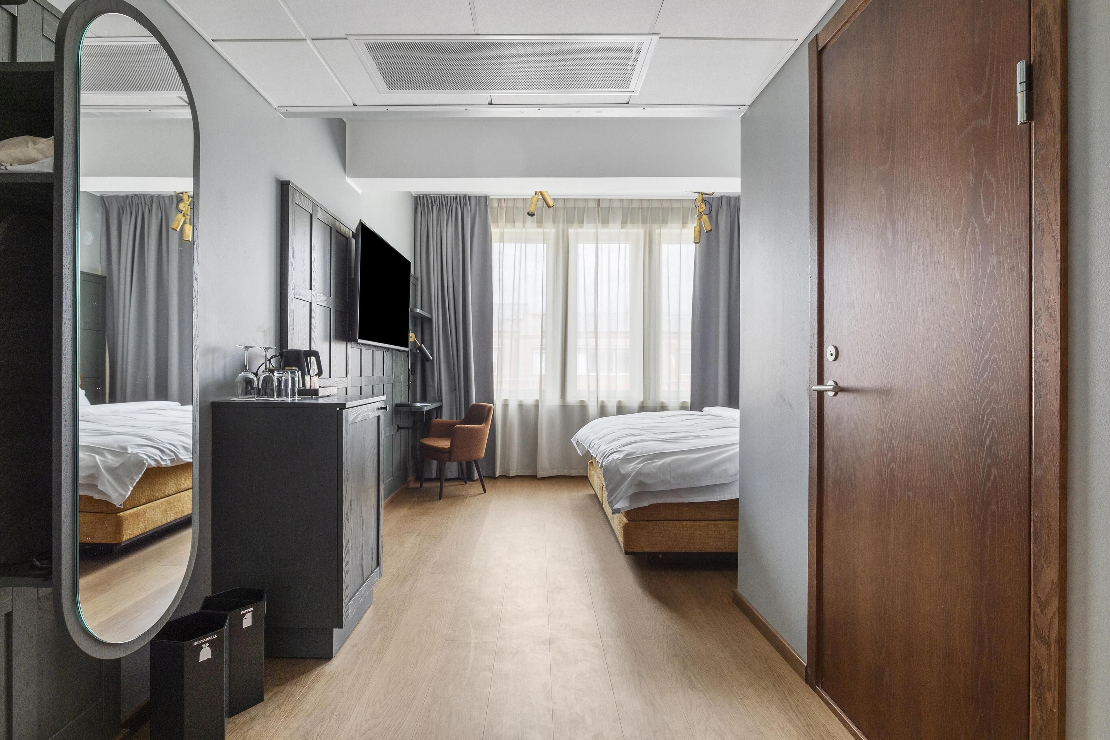 A hotel room with a bed, a desk, a chair, a TV, a mirror, and a wardrobe.