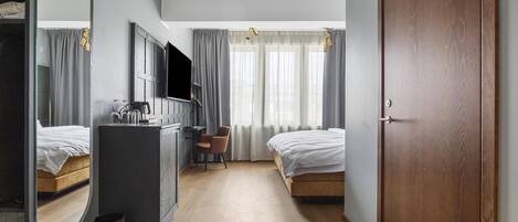 A hotel room with a bed, a desk, a chair, a TV, a mirror, and a wardrobe.