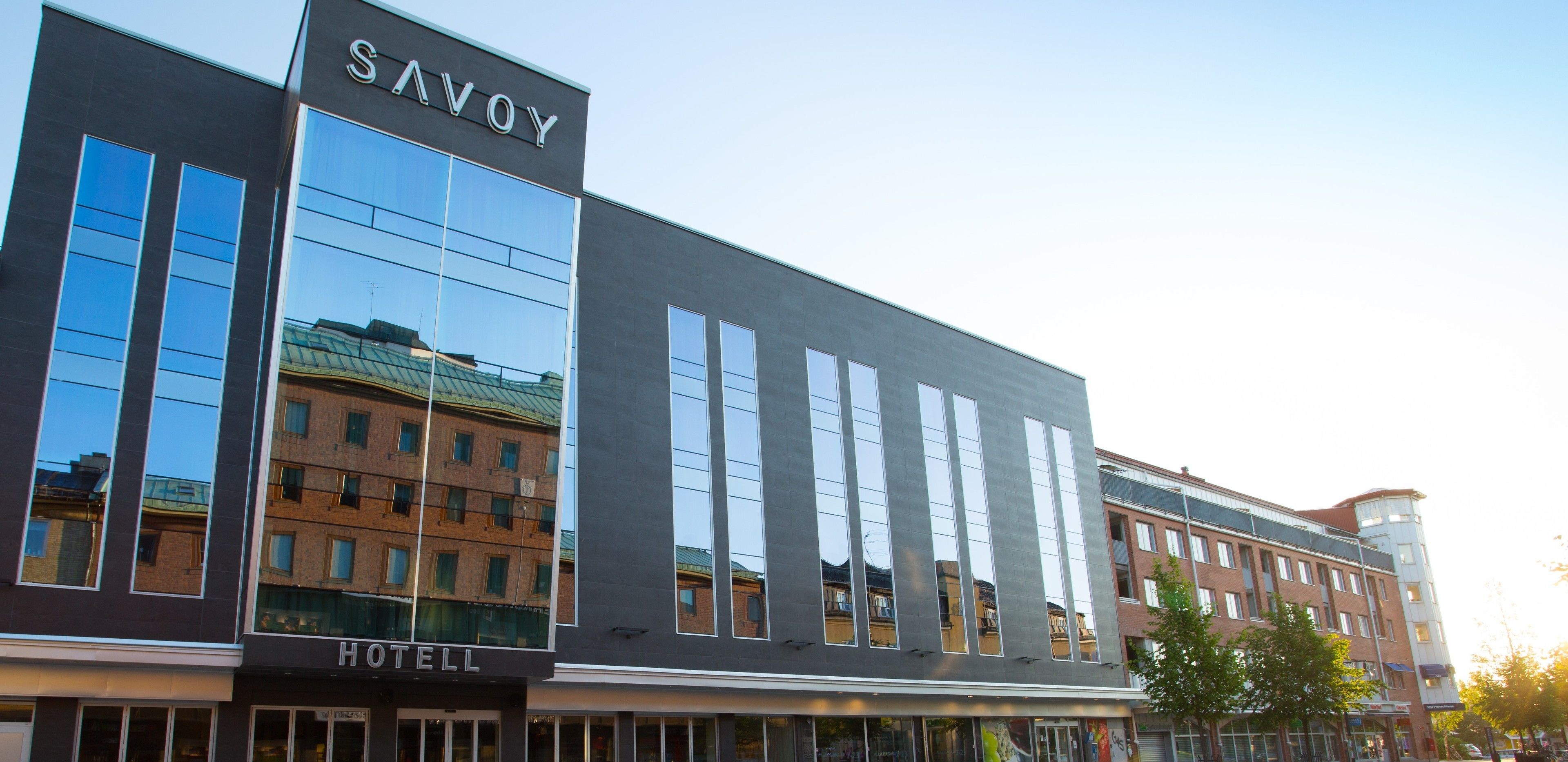 En moderne hotelbygning med en stor glasfacade og et skilt med teksten "SAVOY HOTEL".