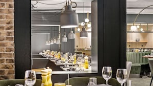 Un restaurante con una larga mesa de comedor dispuesta con copas de vino, platos y cubiertos. Hay lámparas colgantes sobre la mesa y una pared de ladrillo a un lado.
