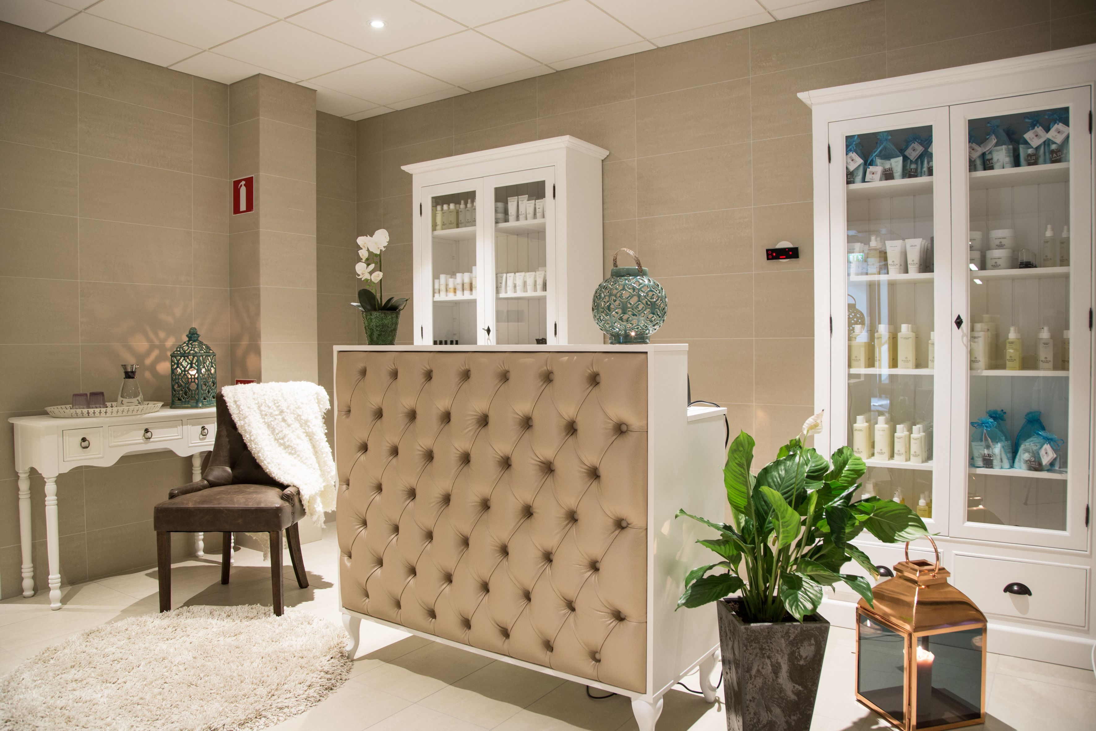 A spa room with a tufted headboard, a white vanity, a cabinet with glass doors, a potted plant, and a candle.