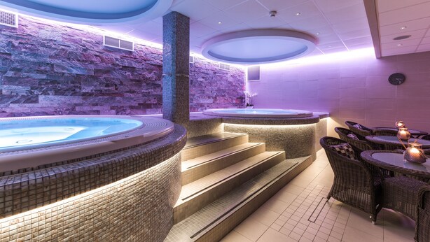 Un área de spa con dos jacuzzis, una pared de piedra y mobiliario de mimbre.