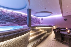 Un área de spa con dos jacuzzis, una pared de piedra y mobiliario de mimbre.