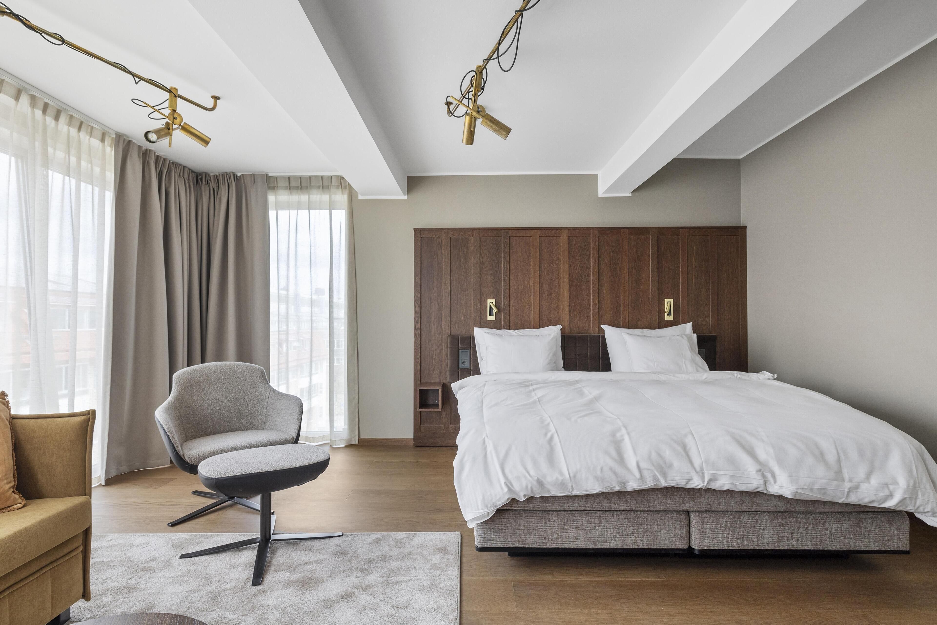 Un dormitorio moderno con una cama grande, una silla, un armario de madera y una lámpara en el techo.