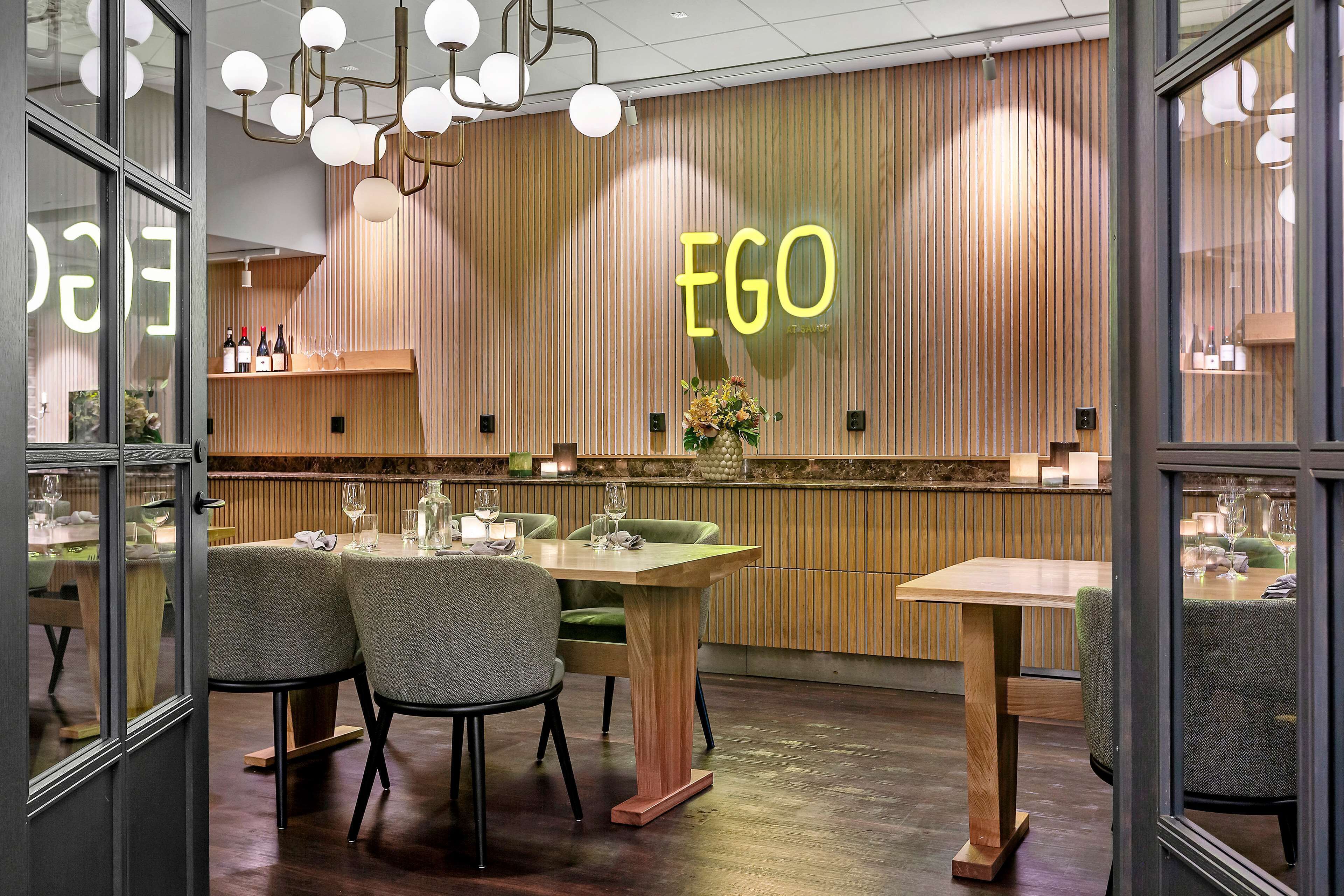 Et restaurantinteriør med træpaneler, et neon 'EGO' skilt og borde dækket til spisning.