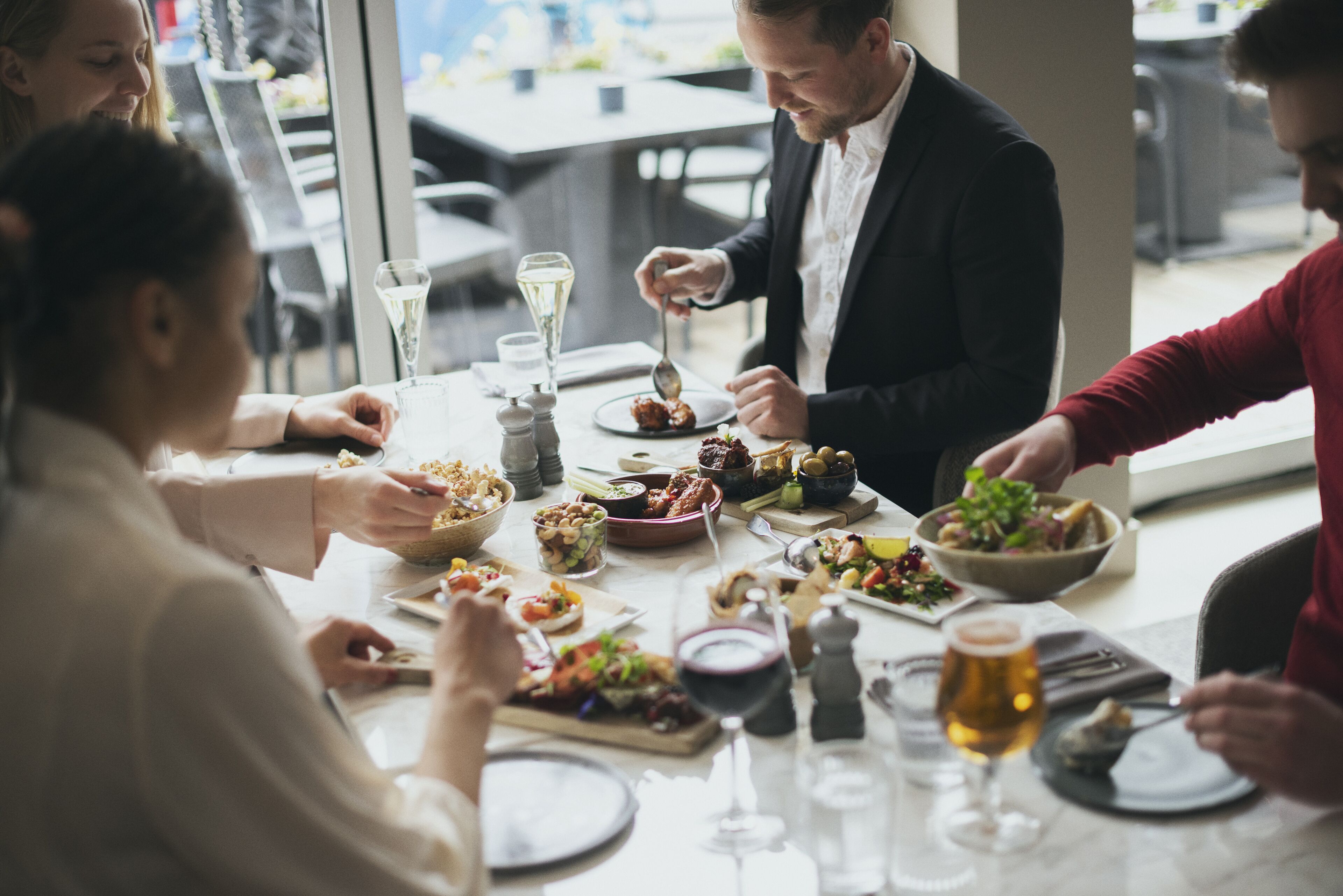 Un grupo de personas comiendo en una mesa con varios platos, copas de vino y un ambiente relajado.