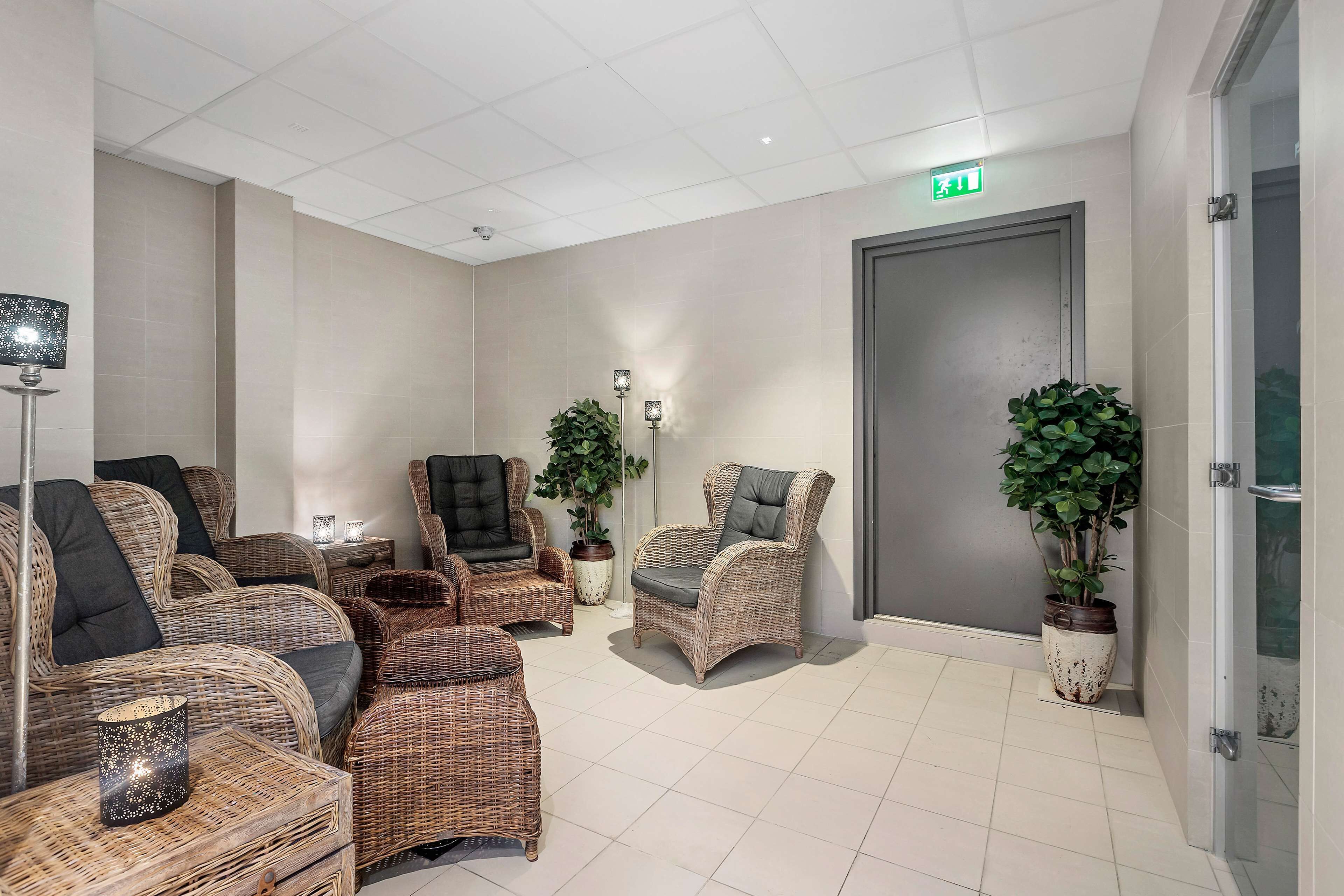 A room with wicker furniture, a green exit sign, and potted plants.