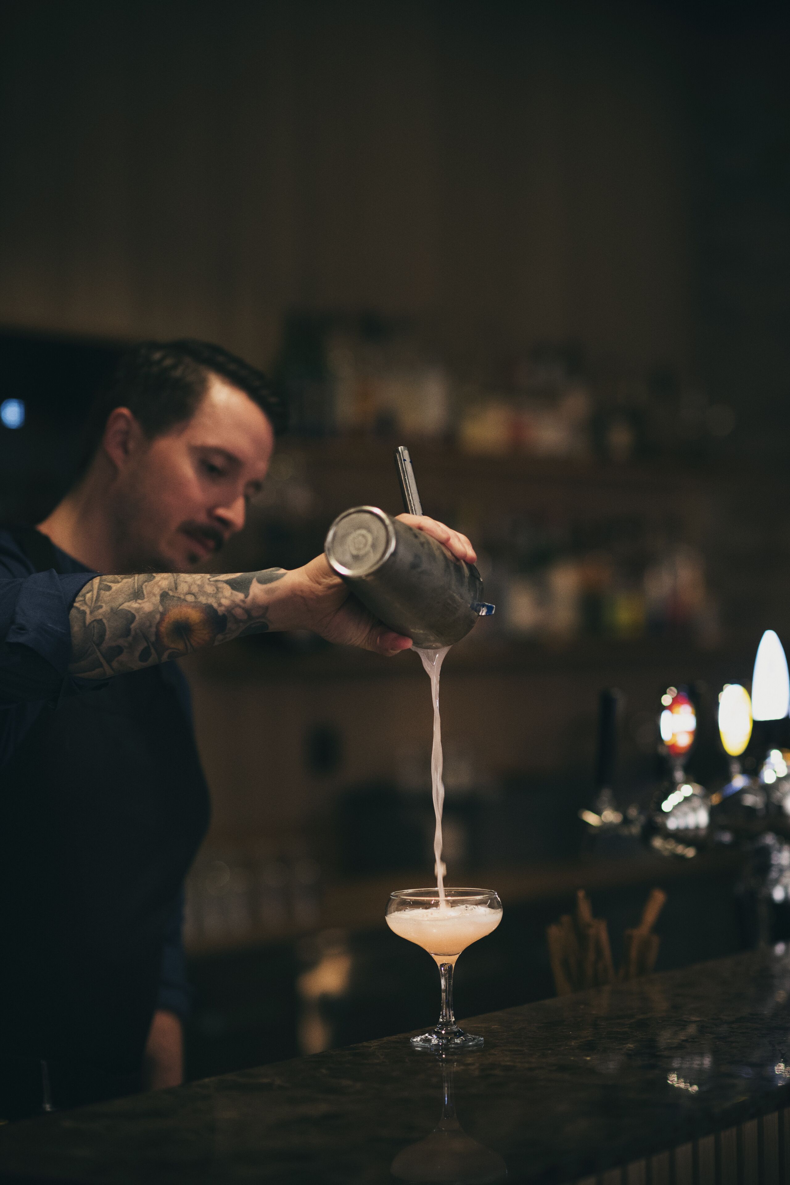 A bartender pouring a drink into a martini glass.
