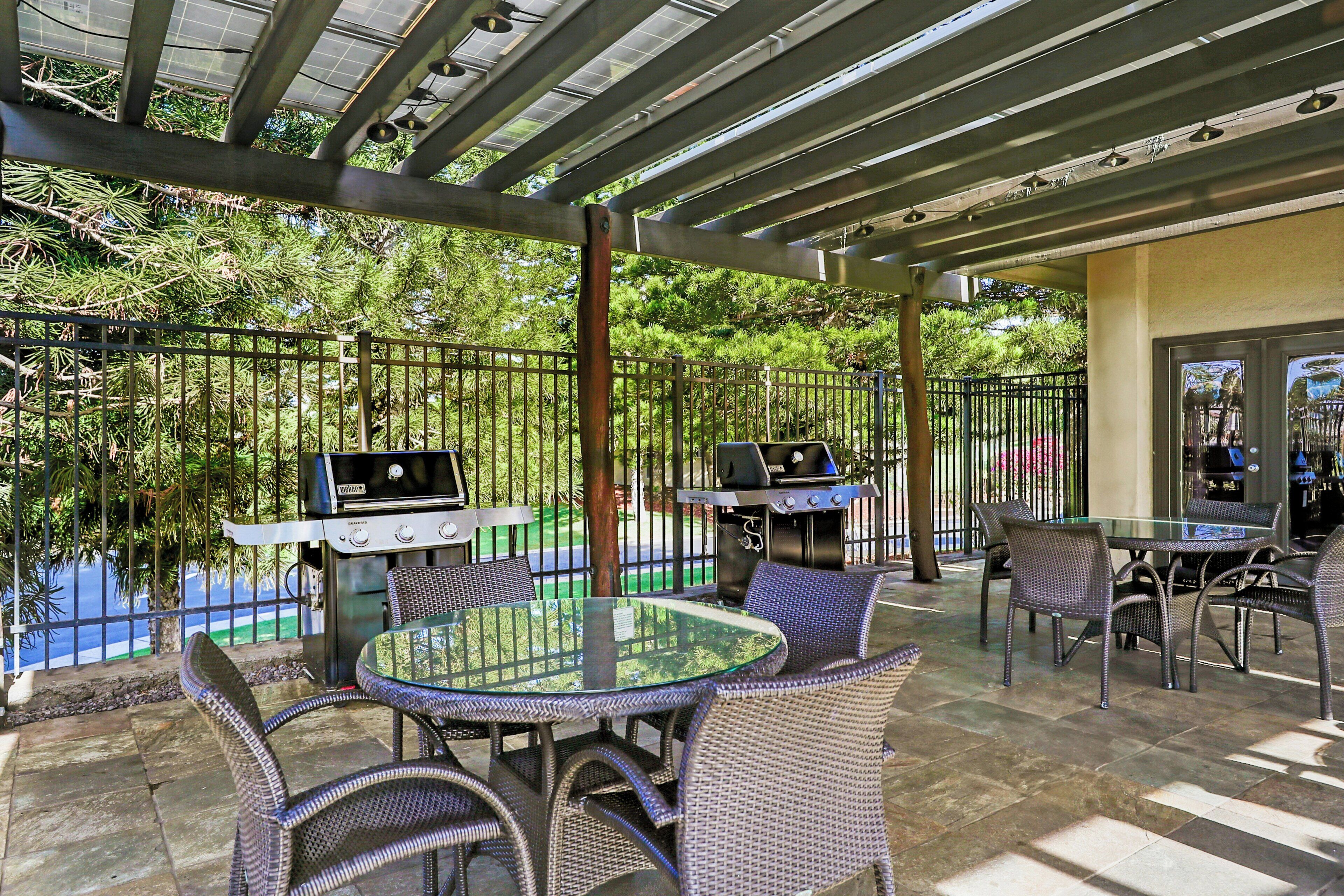 Patio esterno con due barbecue, un tavolo in vetro e sedie in vimini.