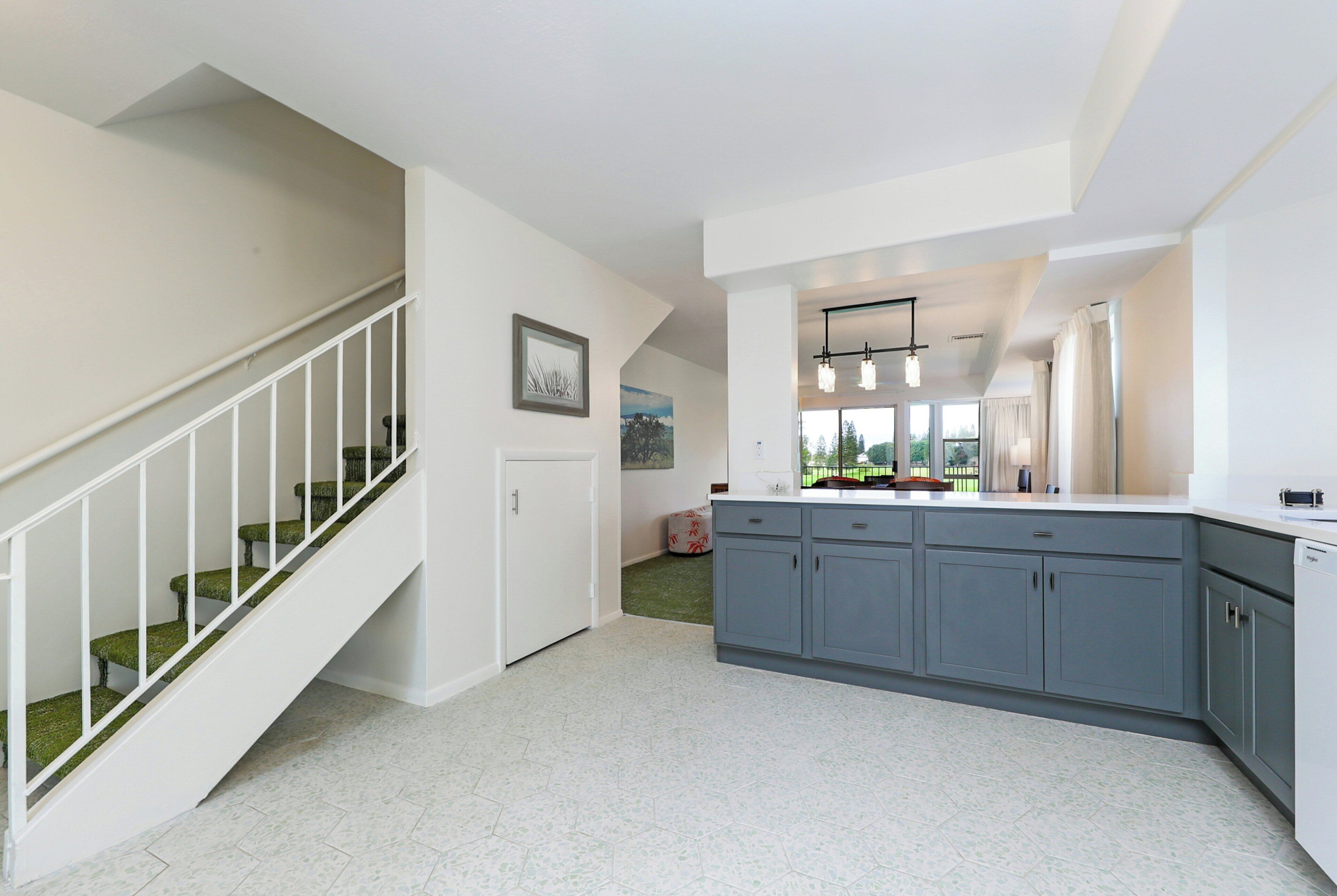 A modern kitchen with grey cabinets, a white countertop, and a staircase with green carpeted steps.