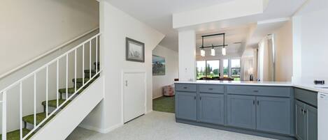 A modern kitchen with grey cabinets, a white countertop, and a staircase with green carpeted steps.