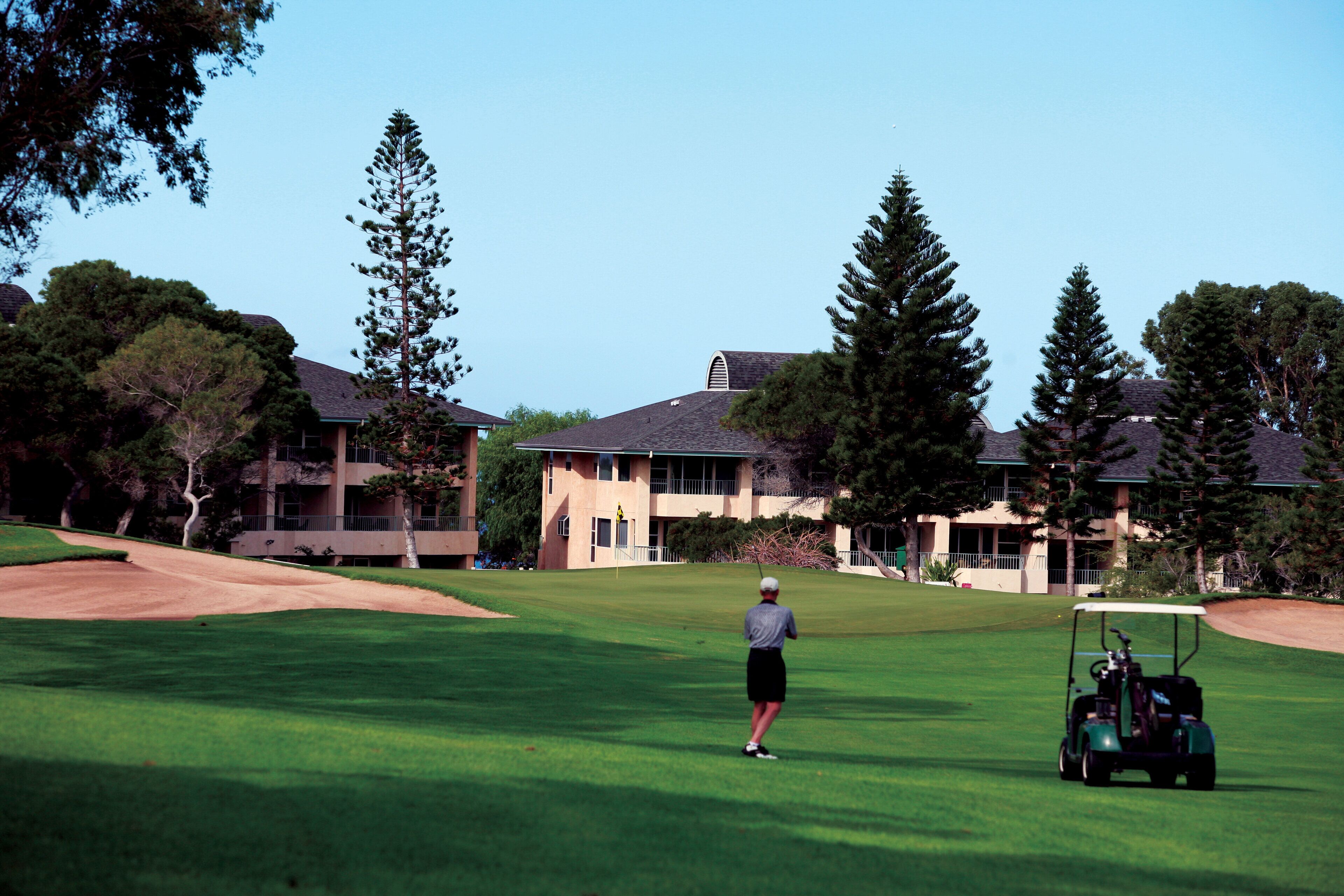 A golf course with a clubhouse and residential buildings in the background.