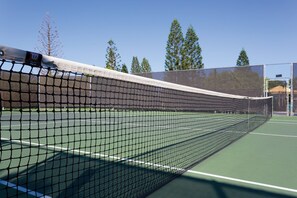 A tennis court with a net in the foreground and trees in the background. - Paniolo Greens At Waikoloa (Waikoloa)