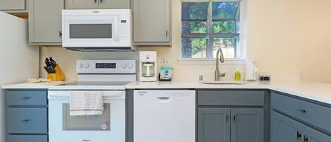 A kitchen with a microwave, oven, dishwasher, and a window with a view of trees.